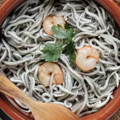 Deliciosas recetas con gulas y gambas, servidas en cazuela de barro con perejil y cuchara de madera.