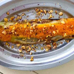 Puerros al horno con salsa picante y frutos secos picados, servidos en un plato metálico.