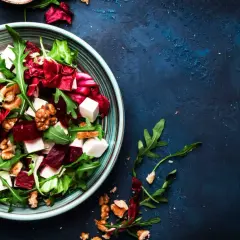 Ensalada de remolacha vibrante con queso feta, nueces y rúcula en un plato azul.