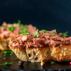 Rebanadas de pan rústico con un generoso untado de paté de hígado de pollo, decorado con perejil fresco y granos de pimienta.