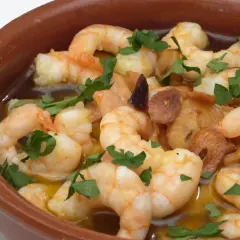 Gambas al pil pil burbujeantes en cazuela de barro, con ajo dorado y perejil fresco.