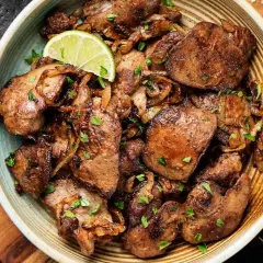 Sabrosos higaditos de pollo encebollados, salpicados de perejil fresco y adornados con rodajas de lima. Un plato casero irresistible.
