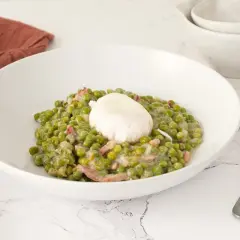 Un plato de guisantes a la francesa cremosos con trocitos de panceta y un huevo escalfado encima.