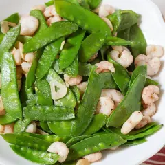 Plato de tirabeques salteados con gambas y ajo. Los tirabeques, crujientes y verdes, se mezclan con las gambas rosadas y láminas de ajo.