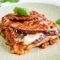Un trozo de parmigiana di melanzane, con capas de berenjena, queso fundido y salsa de tomate, adornado con hojas de albahaca fresca.