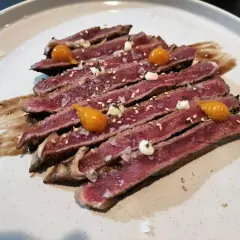 Tataki de ternera, finas lonchas de carne rosada con sésamo, sal gorda y toques de salsa y puré de mango.