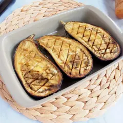 Berenjenas asadas al horno, cortadas por la mitad y con un patrón de rejilla, listas para disfrutar.