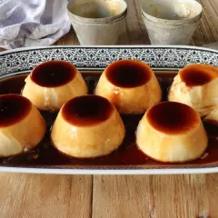 Seis deliciosos flanes de leche condensada, bañados en caramelo oscuro, servidos en una bandeja decorada.