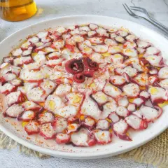 Delicioso carpaccio de pulpo, finas láminas rociadas con aceite de oliva y pimentón, listo para disfrutar.