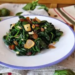 Espinacas a la catalana con pasas, piñones y ajo crujiente en un plato blanco.