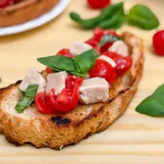 Una bruschetta que es un pan tostado cubierto con tomates frescos, cubos de mozzarella y hojas de albahaca verde.