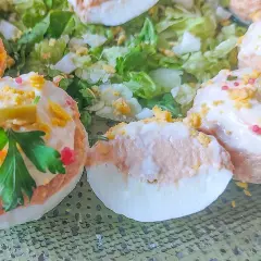 Deliciosos huevos rellenos adornados con aceitunas, perejil y trocitos de huevo duro, servidos sobre una cama de lechuga fresca.