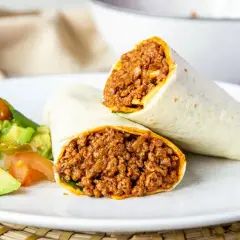 Dos burritos de carne picada, cortados por la mitad, servidos con una ensalada fresca de aguacate y tomate.