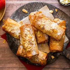 Deliciosos rollos de strudel de manzana dorados, espolvoreados con azúcar glas y almendras fileteadas, listos para disfrutar.