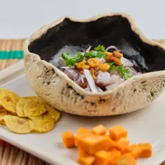 Delicioso ceviche de corvina en cuenco rústico, acompañado de patacones y cubos de camote.