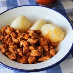 Plato de zorza con patatas, servido en un cuenco blanco con borde azul sobre un mantel de cuadros azules.