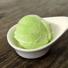 Una bola de helado de manzana verde en un cuenco blanco sobre una mesa de madera.