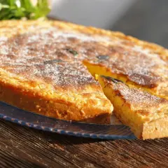 Un delicioso postre típico de Ibiza, una tarta dorada espolvoreada con azúcar glas, con una porción cortada.