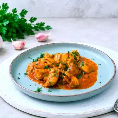 Sabroso pollo al curry con perejil picado, servido en un plato azul. Acompañado de ajos y un manojo de perejil fresco.
