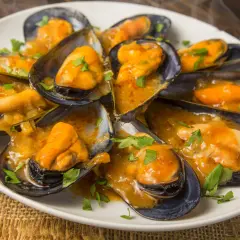 Mejillones en salsa, como los de los bares, servidos en una cazuela blanca con perejil picado.