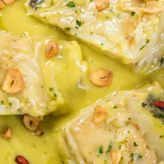 Merluza al pil pil, jugosos trozos de pescado blanco en una salsa cremosa con láminas de ajo crujiente y guindilla.