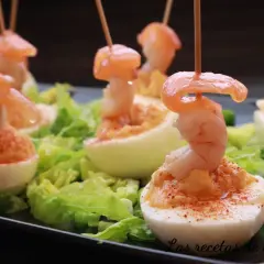 Huevos rellenos espectaculares adornados con camarones y pimentón, servidos sobre lechuga fresca.