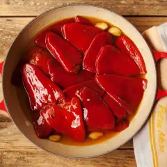 Pimientos del piquillo asados en una cazuela roja, con ajos y un paño de cocina.
