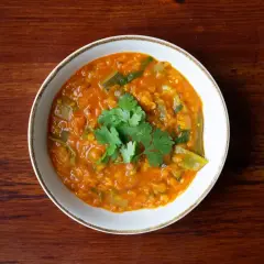 Un tazón de lentejas al curry, con cilantro fresco, servido sobre una mesa de madera.