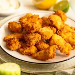Plato de lagrimitas de pollo crujientes, acompañadas de rodajas de pepino y limón.