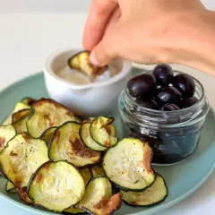 Crujientes rodajas de calabacín en airfryer, servidas con aceitunas negras y una salsa para mojar.