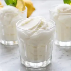 Tres vasos de sorbete de limón, refrescante y cremoso, con limones amarillos y hojas de menta al fondo.