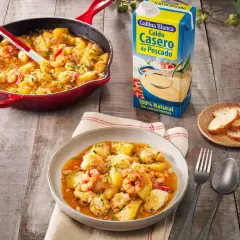 Delicioso rape a la marinera con patatas y gambas, servido en plato y sartén, junto a caldo de pescado y pan.