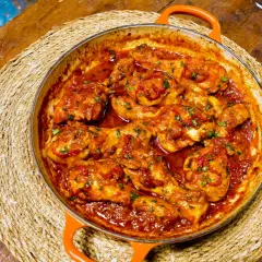 Pollo a la toledana en cazuela naranja, servido sobre una esterilla de mimbre en una mesa de madera rústica.