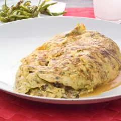 Tortilla de bacalao vasca, esponjosa y dorada, servida en plato blanco sobre mantel rojo.