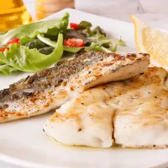 Deliciosa merluza a la plancha con piel crujiente, acompañada de ensalada fresca y un gajo de limón.