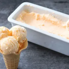 Un cono con tres bolas de helado de melón cremoso y una cubeta llena de este refrescante postre.
