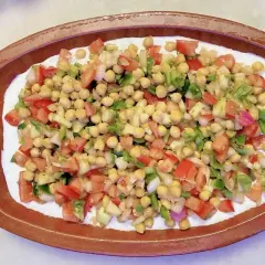 Deliciosa ensalada de garbanzos con tomate, pimiento y cebolla, servida sobre una base cremosa en un cuenco de barro.