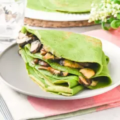 Deliciosos crepes de espinacas rellenos de champiñones salteados, servidos en un plato gris con un tenedor al lado.