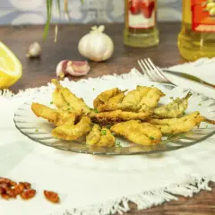 Un plato de boquerones en adobo crujientes, servidos con limón, ajo y guindillas.