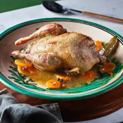 Perdiz a la toledana servida en plato decorado con rodajas de zanahoria y especias.