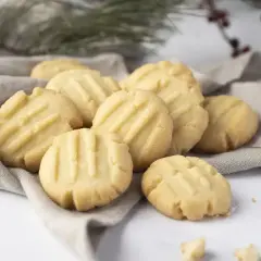 Montón de galletas de mantequilla doradas con líneas marcadas, servidas sobre una tela gris.
