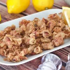 Crujientes puntillas de calamar fritas en un plato blanco, acompañadas de limón, aceite y saleros.