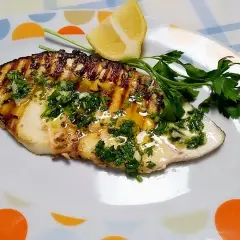 Delicioso emperador a la plancha con perejil fresco, ajo y limón, servido en un plato blanco con círculos de colores.