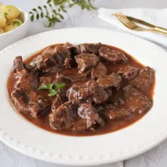 Delicioso morcillo de ternera estofado en salsa, servido en plato blanco con patatas cocidas y perejil picado.
