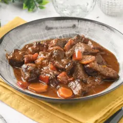 Un plato humeante de carne al toro, tierno y jugoso, con trozos de zanahoria y pimiento en una rica salsa.