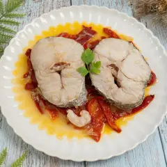 Dos rodajas de merluza a la riojana, servidas sobre pimientos rojos y una gamba, decoradas con perejil.