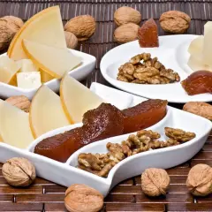 Queso y nueces acompañan trozos de dulce de manzana en una tabla de madera.