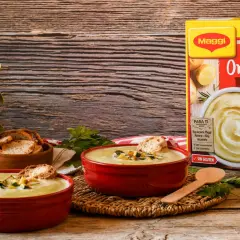 Dos cuencos rojos con cremoso puré de patatas Maggi, tostadas y hierbas. Caja de puré de patatas al lado.