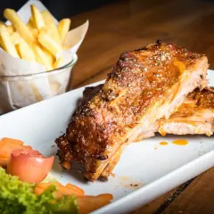 Costillas de cerdo al horno jugosas y doradas, acompañadas de papas fritas crujientes y una guarnición fresca.
