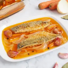 Dos filetes de caballa en escabeche, con zanahoria, cebolla y ajos en una salsa dorada.